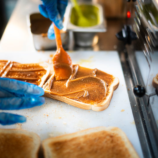 Person spreading Kaya jam on toast with a spatula, wearing blue gloves.