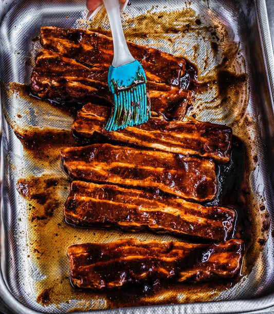 Baked ribs being brushed with Mei Mei spicy soy sauce