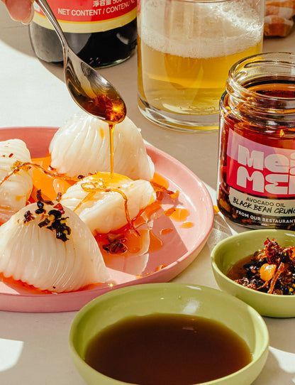 white dumplings, a jar of Meiji black bean crunch, and a spoon drizzling the sauce. 