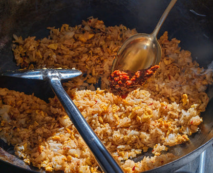 Cooked rice with a spoon adding Sambal Chilli paste to a wok.