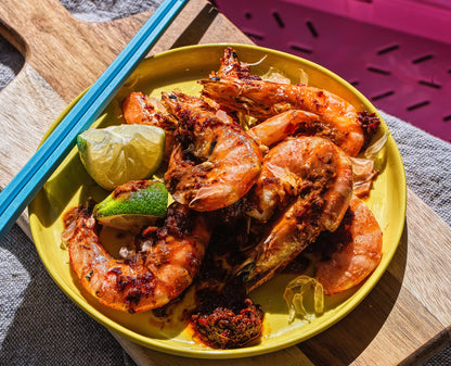 Grilled shrimp with Mei Mei Sambal Chilli paste, lime wedges, and a wooden cutting board.