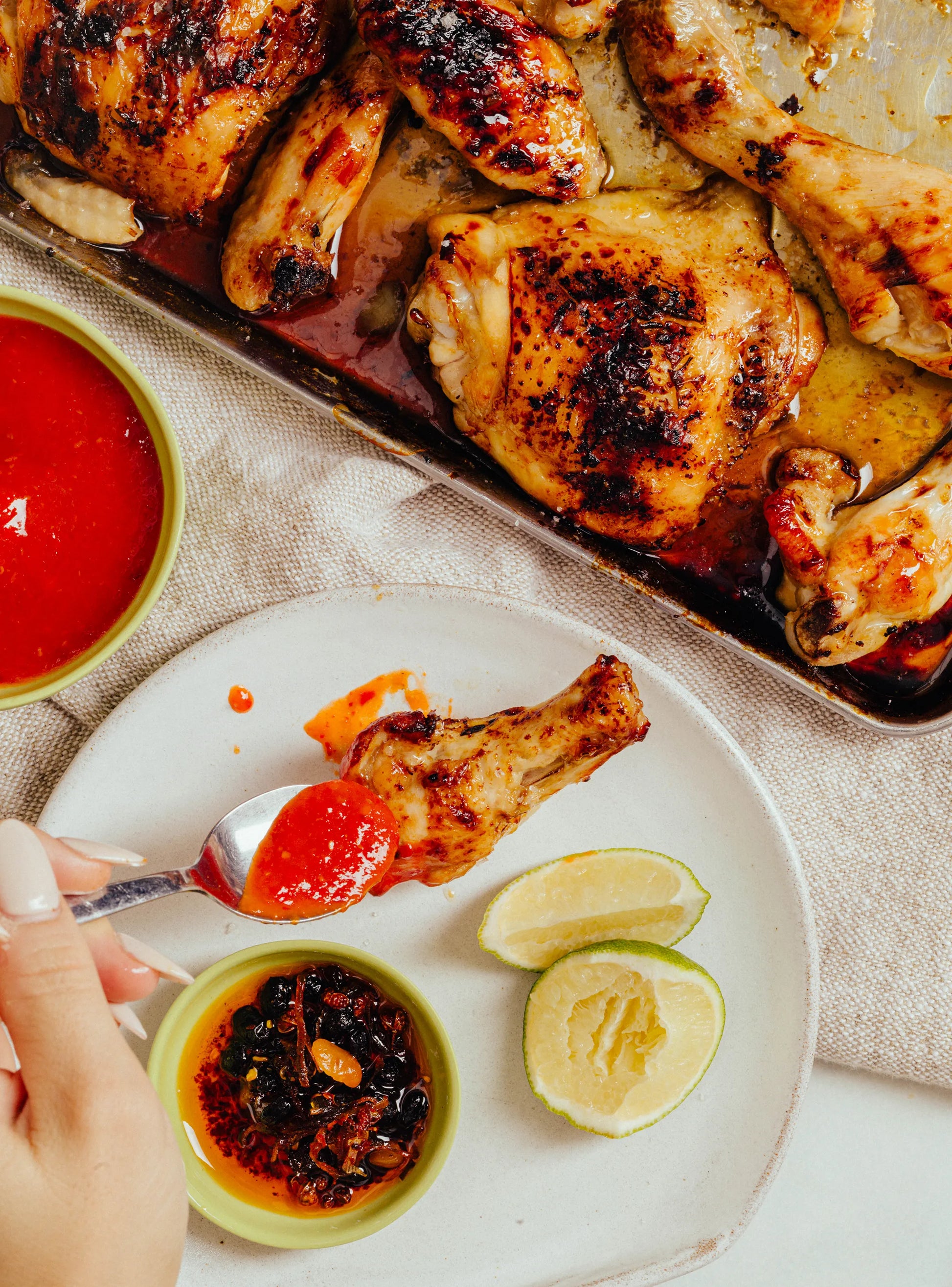 Baked chicken with a side of Mei Mei House Chilli sauce and lime wedges on a white plate.