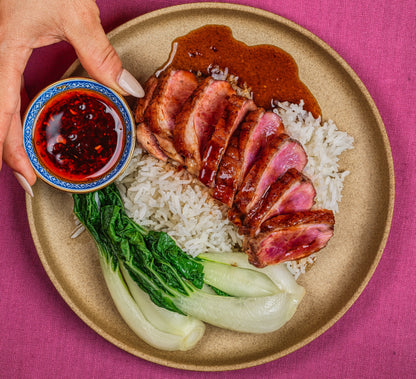 Sliced roasted duck with rice and greens on a plate with a hand holding a small bowl of MEI MEI condiments 
